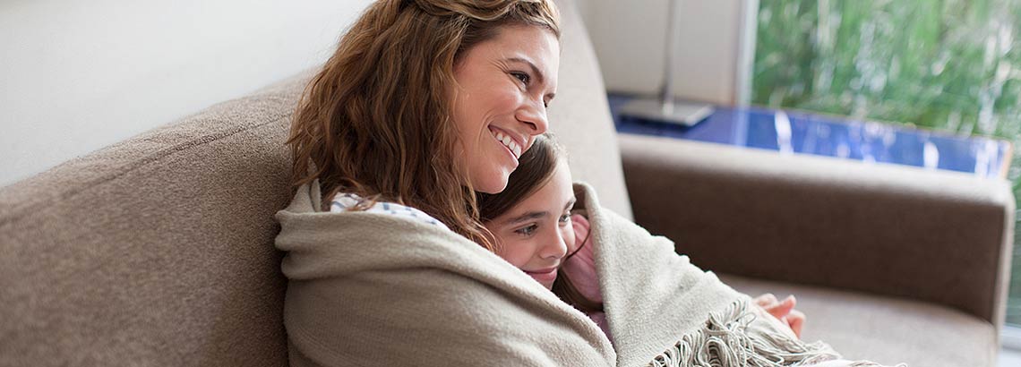 Frau mit Tochter in Decke eingewickelt auf dem Sofa