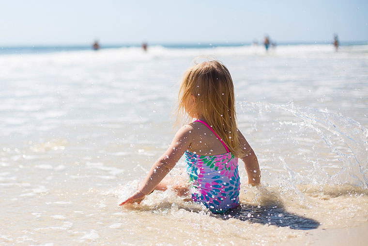 Kleines Kind sitzt am sonnigen Strand am Meer