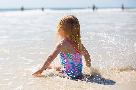 Kleines Kind sitzt am sonnigen Strand am Meer