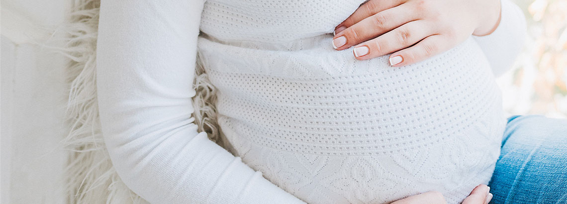 Nahaufnahme des Bauchs einer schwangeren Frau mit weißem Shirt